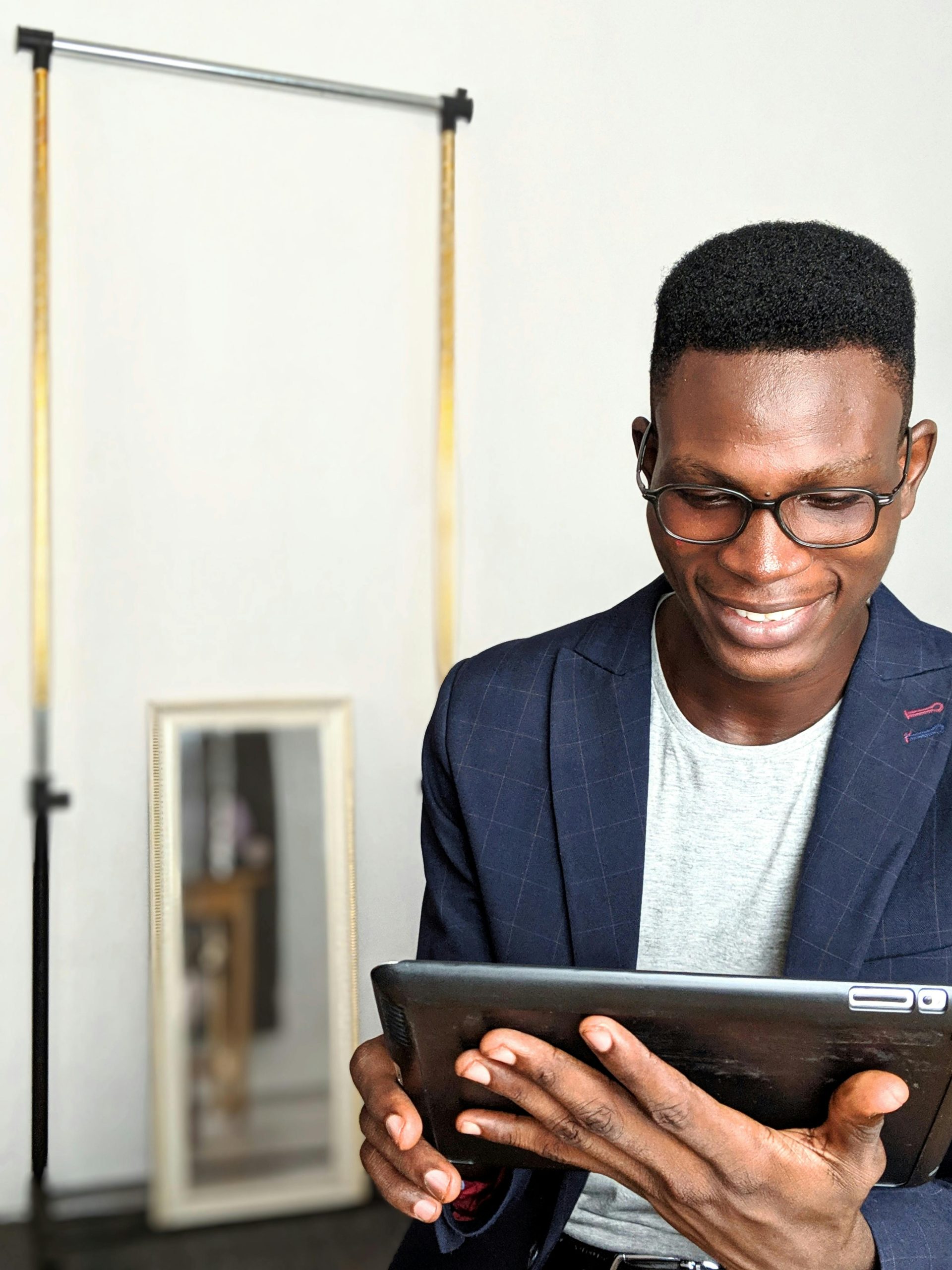 Portrait of a young man in a blazer using a tablet indoors, smiling and enjoying the moment.